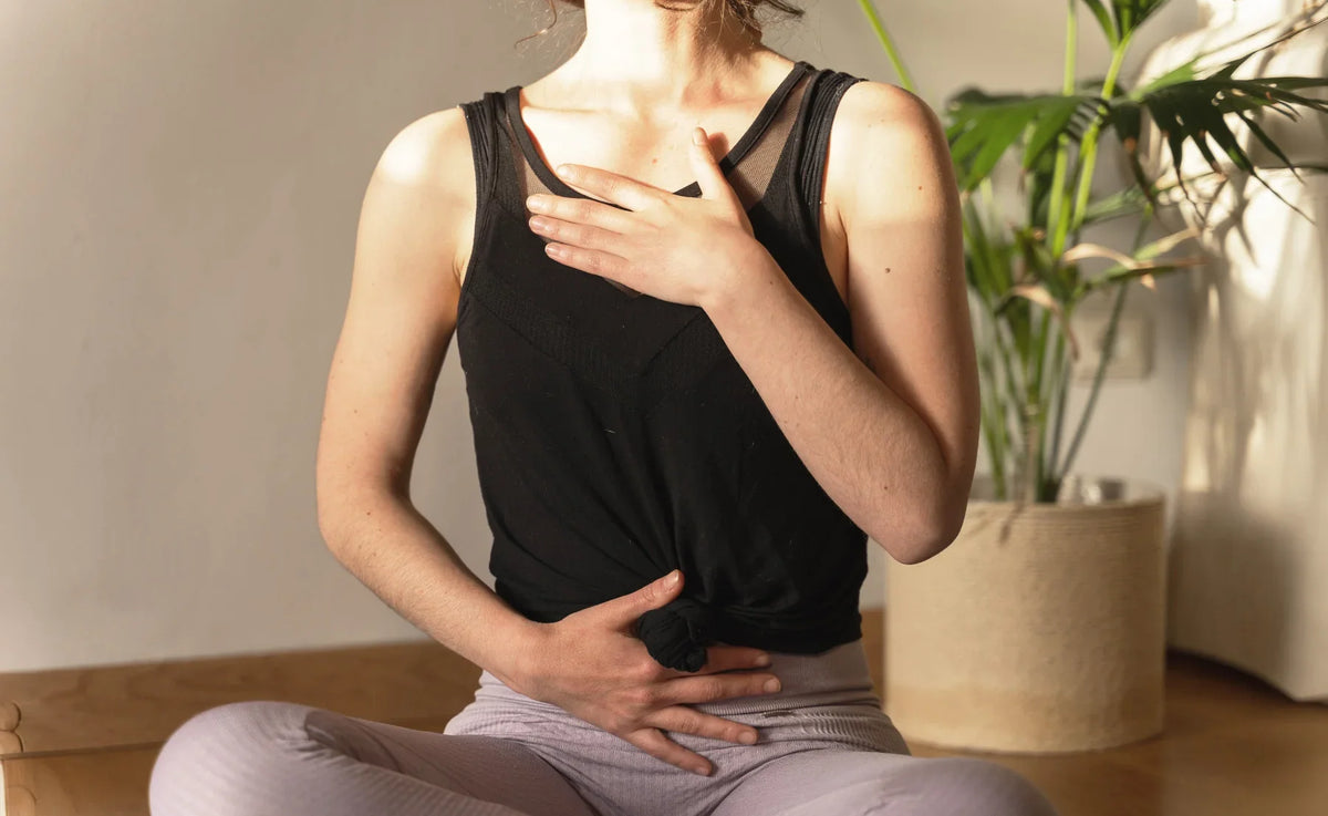 Woman sitting cross-legged holding her chest and abdomen, experiencing digestive or chest discomfort.