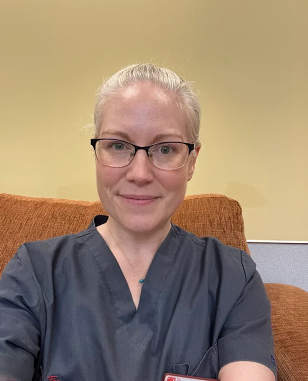 A smiling female practitioner in grey medical scrubs against a neutral background.