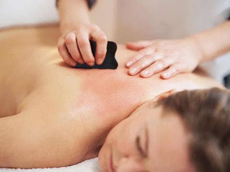 A therapist performing Gua Sha treatment on a person's back using a black scraping tool.